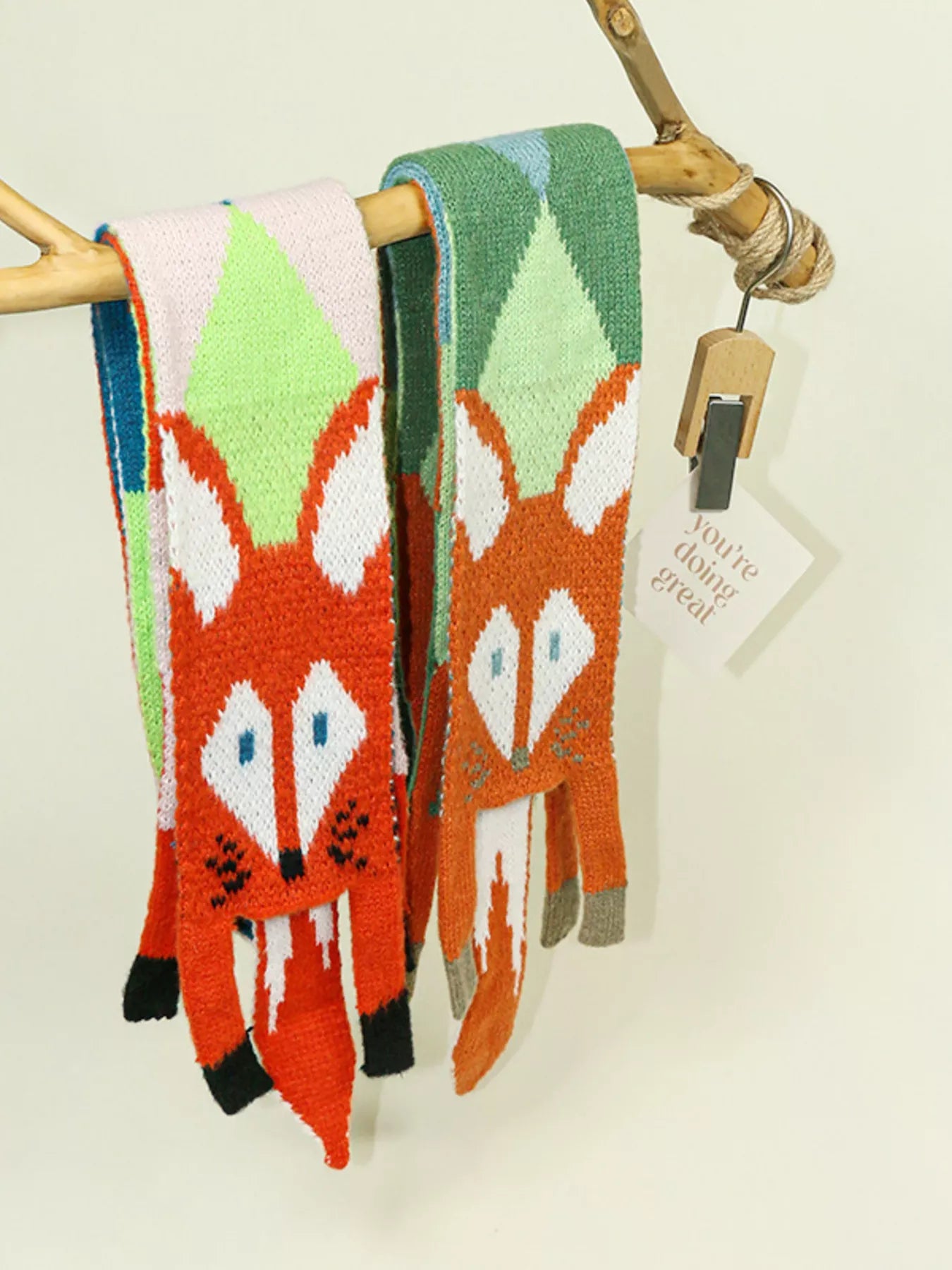 Two fox-patterned scarves hanging on a wooden rack with a tag.