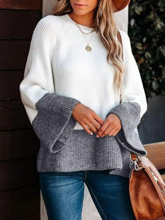 Woman wearing a white sweater with gray bell sleeves, blue jeans, and holding a brown bag.