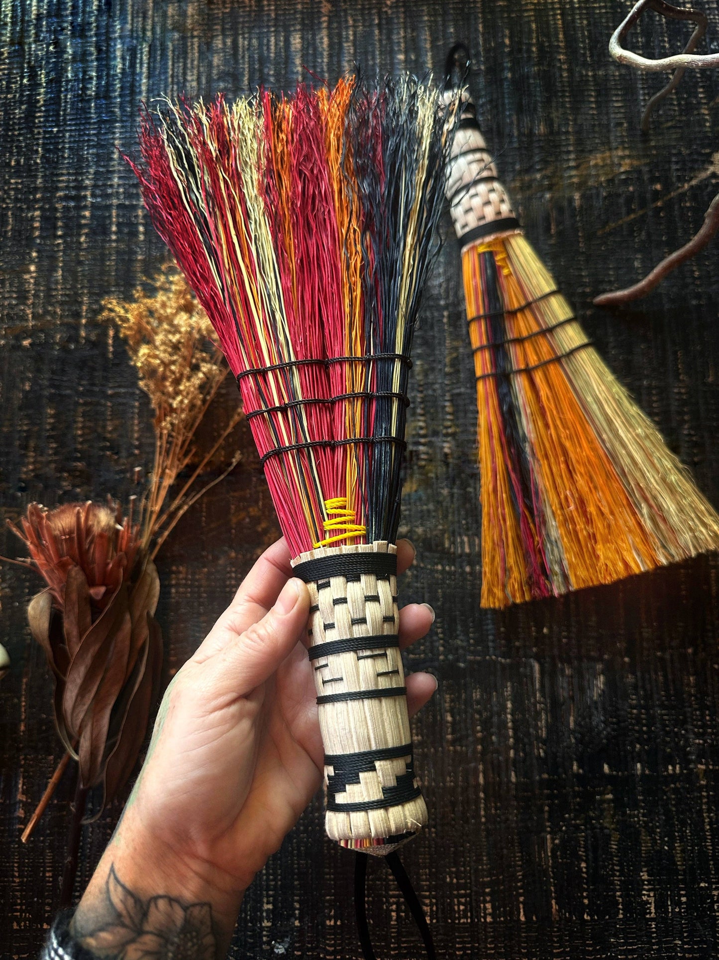 Hand holding a colorful broom with another broom in the background on a textured surface.