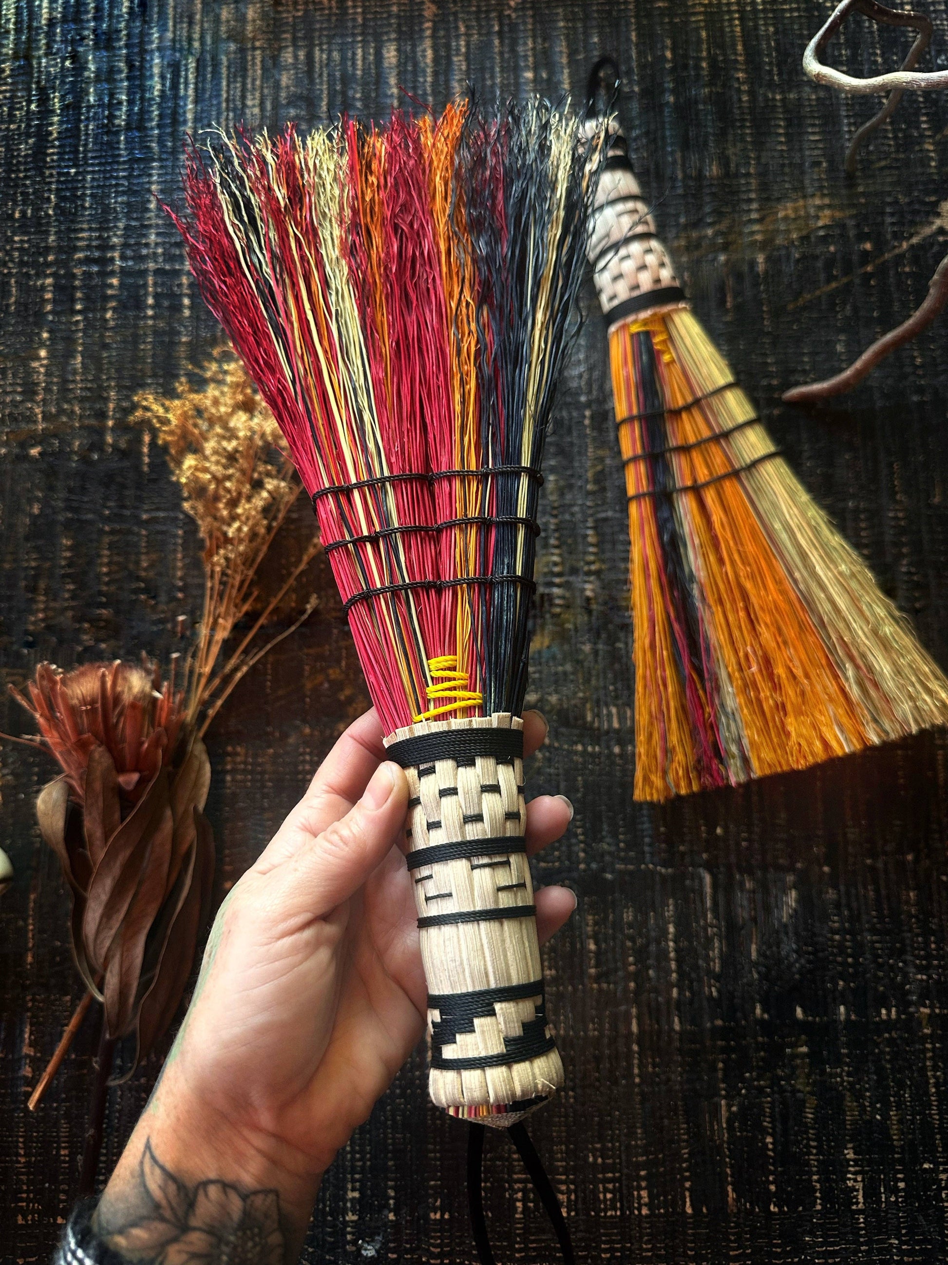 Hand holding a colorful broom with another broom in the background on a textured surface.
