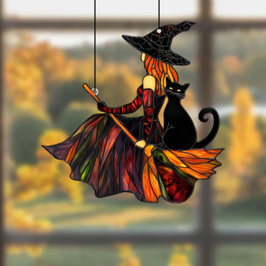 Decorative acrylic stained glass witch and black cat on a broom hanging against a blurred autumn window background.