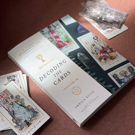 Book titled 'Decoding the Cards' by Sheila Ellis with tarot cards on a brown surface