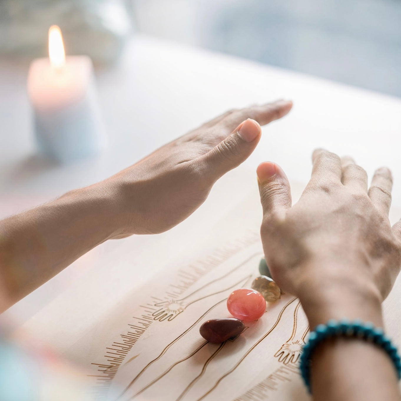 Two hands reaching towards each other over a wooden surface with stones and a lit candle in the background.